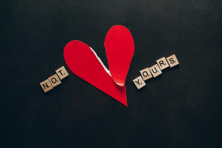 A torn red heart with 'Not Yours' spelled in Scrabble tiles on a black background.